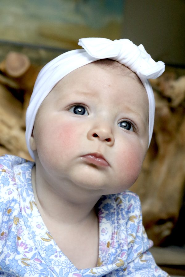 A baby in a white knotted headband and floral top looking up