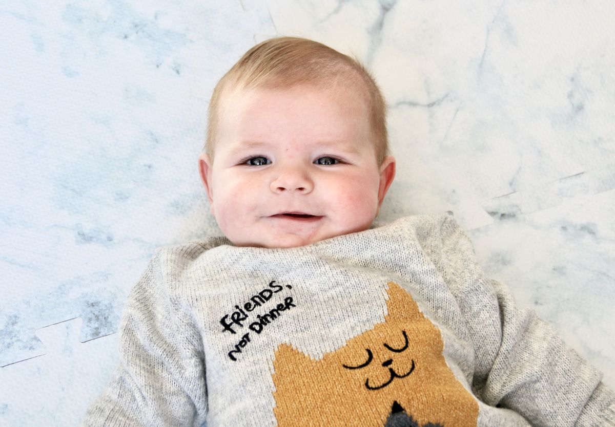 A smiling baby in a grey knitted jersey lying on a marble-print mat