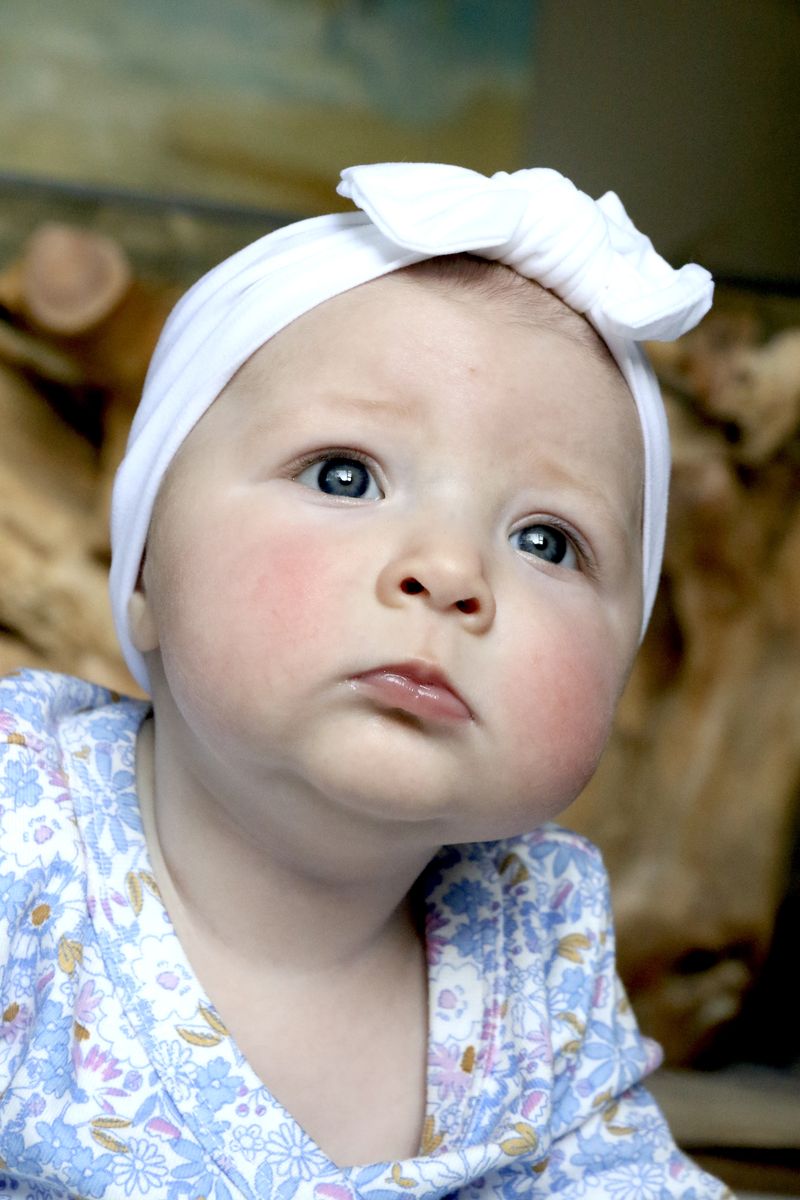 A baby in a white knotted headband and floral top looking up