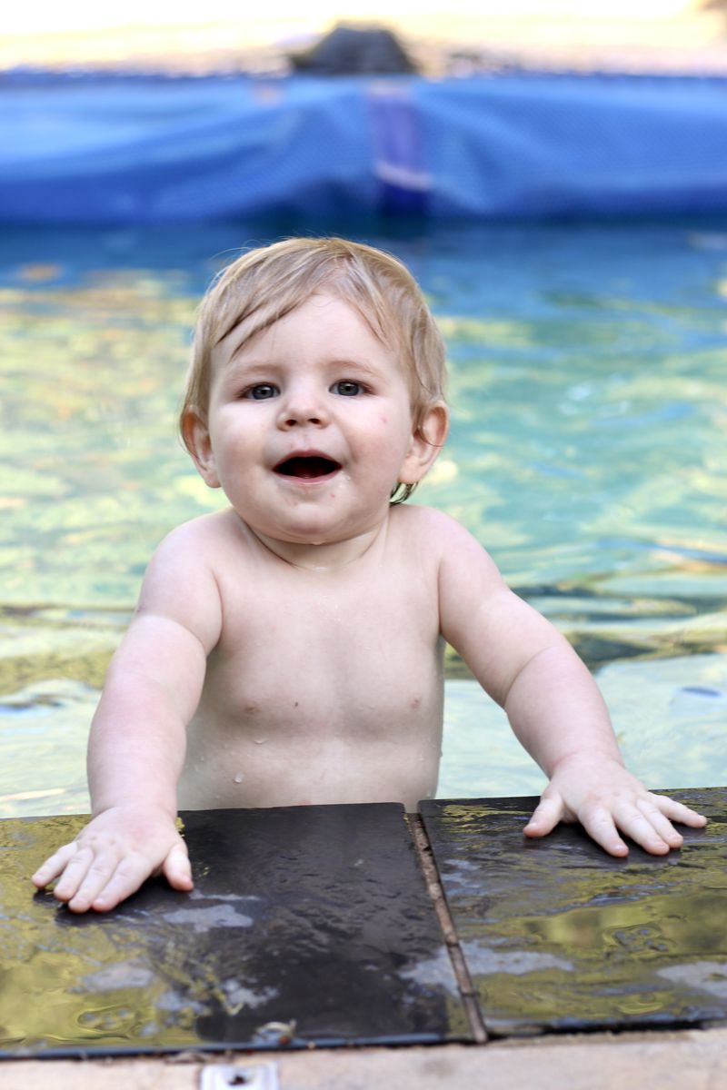 A wet, happy toddler holding on to the edge of a swimming pool