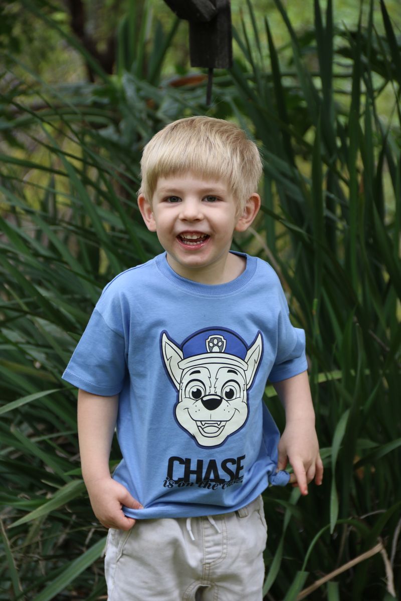 A laughing blond boy in a blue T-shirt standing in the garden