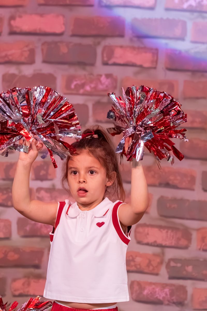 A girl on stage holding red and silver pom-poms high above her head