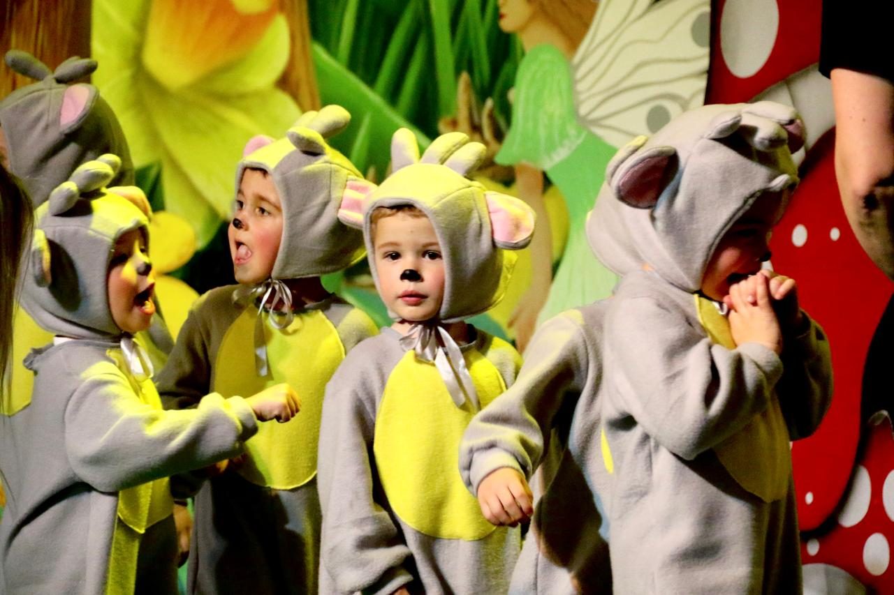 Young children in grey and yellow mouse costumes singing together on stage