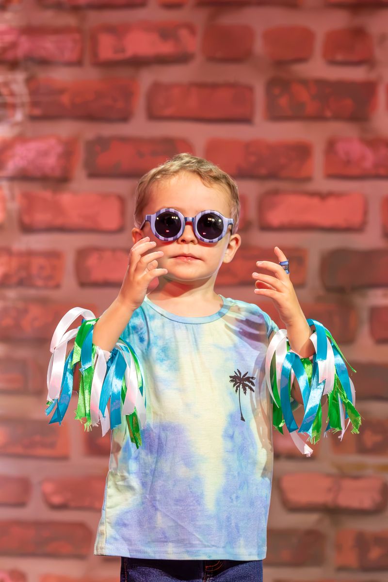 A boy in round sunglasses and ribbon cuffs dancing on stage